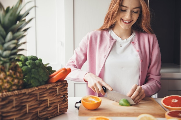 A person holding a variety of fresh fruits and vegetables known to be high in vitamin C, such as oranges, kiwi, and broccoli. The background is a brightly lit kitchen.