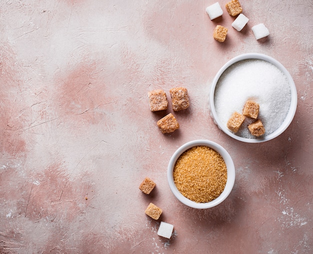 An overhead shot comparing the textures and colors of brown sugar and white sugar side-by-side in small glass bowls.