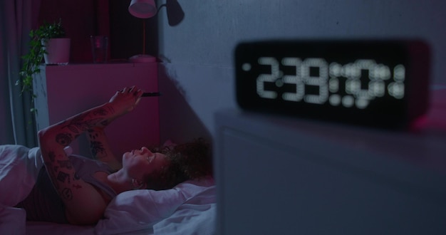 A person tossing and turning in bed at night, unable to fall asleep. The room is dark, but there is a faint glow coming from a digital clock showing 3:00 AM. The person looks frustrated and tired.