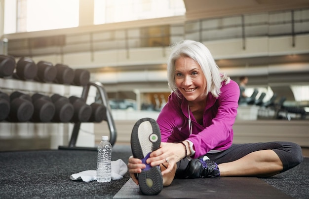 A woman in her 40s doing squats with dumbbells in a gym. She is smiling and looks strong and healthy. She is wearing athletic clothes and the gym is well-lit and modern.