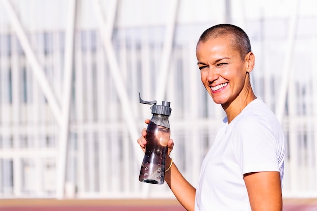 A person holding a reusable water bottle filled with sparkling water, with a backdrop of a gym or yoga studio, illustrating the importance of hydration during physical activities.