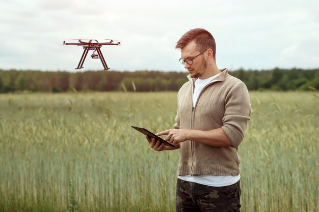 A farmer using a tablet to analyze data collected by a drone flying over a soybean field. The tablet displays a detailed map of the field, showing areas with different levels of plant health, fertilizer status and water stress.