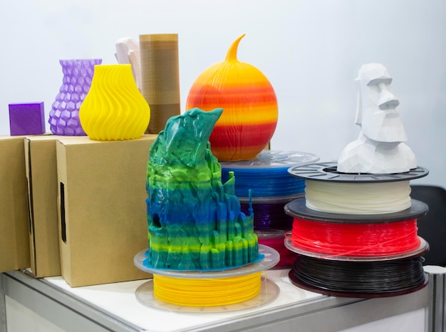A close-up shot of different types of 3D printing filaments (PLA, ABS, PETG) arranged neatly on a shelf, with labels clearly visible. In the background, a partially assembled 3D printer is visible.