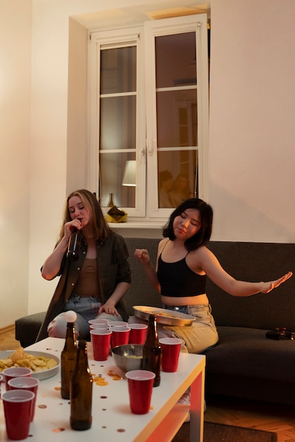 Two friends laughing while watching a movie on a portable projector screen in a living room. The projector is placed on a coffee table, and the screen is set up against a wall. The room is dimly lit, creating a cozy and inviting atmosphere.