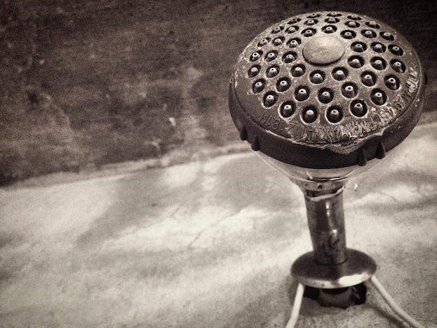 A close-up of an antique electric showerhead, showcasing its metallic components, wiring, and the simple mechanism for water flow. Include some rust or signs of wear to emphasize its age.