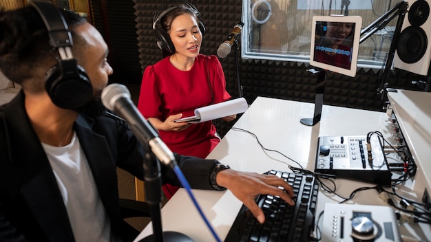 Broadcasters in a radio station booth during a live broadcast, filled with mixing equipment, monitors, and microphones.